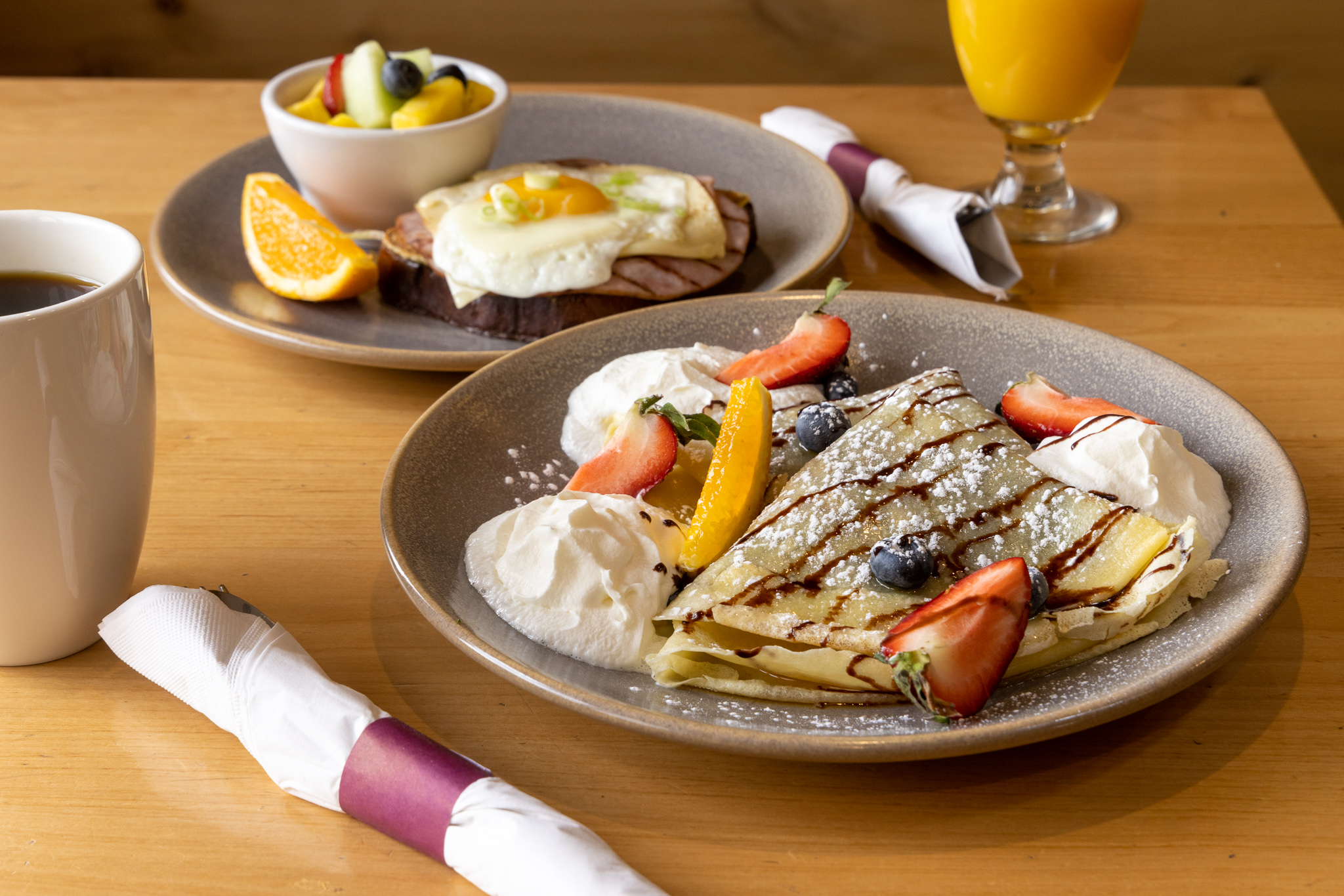Breakfast table with crepes, orange  juice, coffee, and over easy eggs with a fruit cup